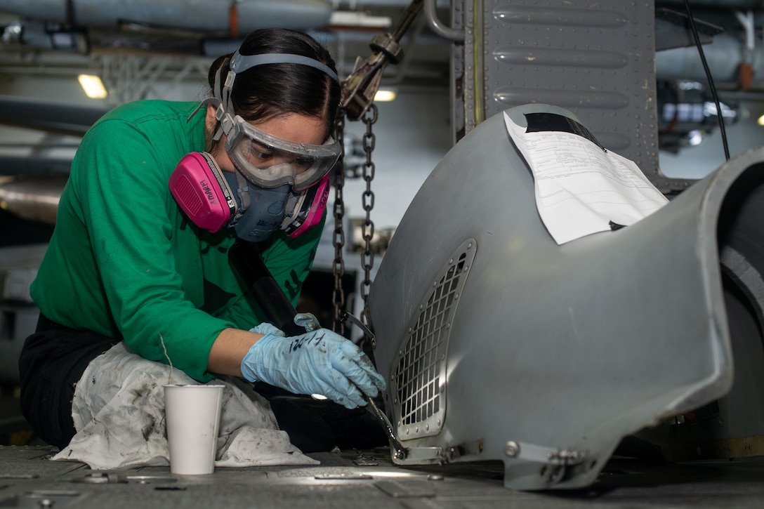 A service member paints an engine cover.
