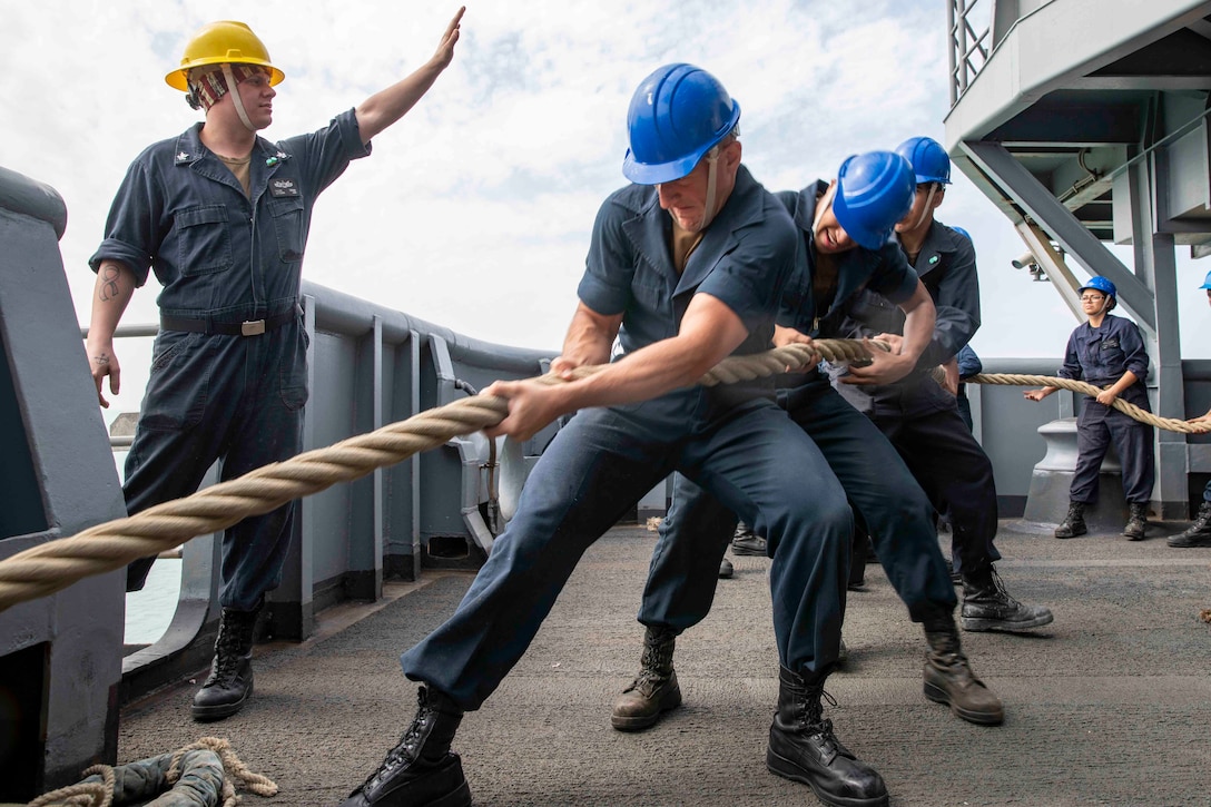 Sailors pull a line as a ship arrives at a port.