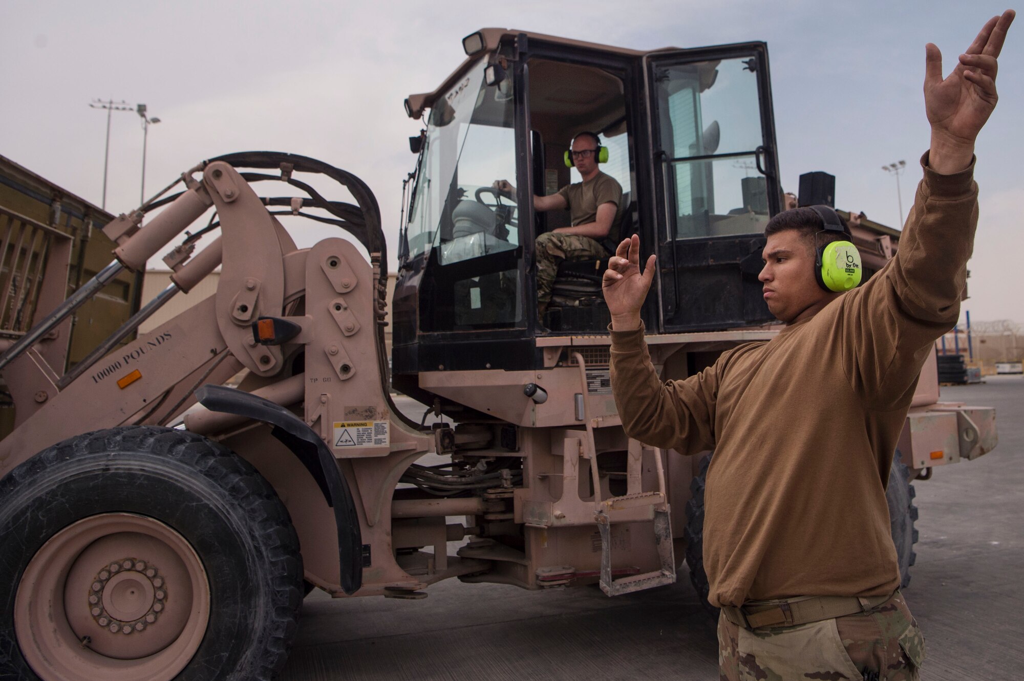 Airman Dylan Durham, 379th Expeditionary Logistics Readiness Squadron (ELRS) traffic management office (TMO) traffic management apprentice, acts as a ground guide for Senior Airman Nicholas Mote, 379th ELRS TMO traffic management journeyman, during the movement of a shipping container Feb. 22, 2019, at Al Udeid Air Base, Qatar. The 379th ELRS TMO handles the pick-up, storage, shipment, and delivery of assets such as small vehicle parts, aircraft engines, and clothing items throughout the U.S. Central Command area of responsibility. (U.S. Air Force photo by Tech. Sgt. Christopher Hubenthal)