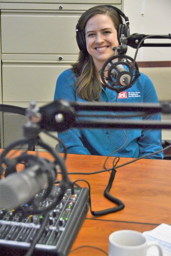 Woman in blue shirt sits in front of audio recording mixer board with headphones on