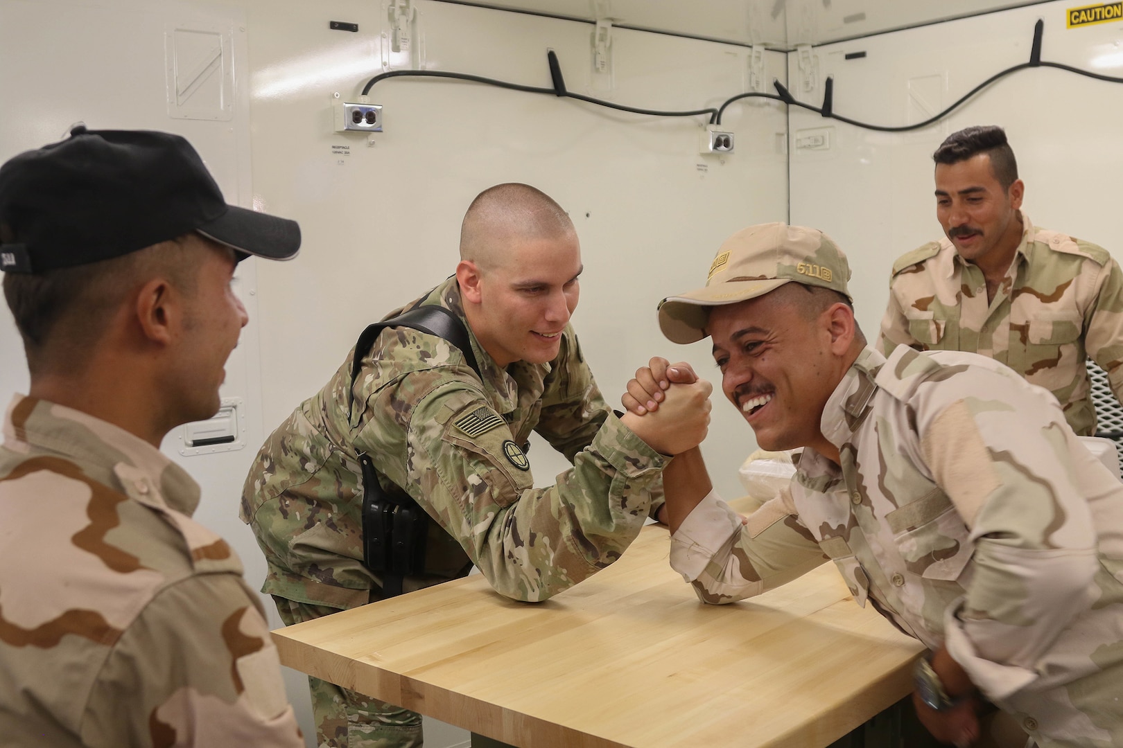 U.S. Army Staff Sgt. David Johnson, the powertrain shop chief assigned to B Company, 935th Aviation Support Battalion, Illinois Army National Guard, arm wrestles with an Iraqi aviation engineer during a break from organizing the portable maintenance shop containers at an Iraqi hangar at Camp Taji Military Complex, Oct. 1, 2018.  The Iraqi Air Enterprise will ultimately provide Iraq with the self-sufficient air capabilities required by a sovereign nation to protect its borders and defeat internal threats.