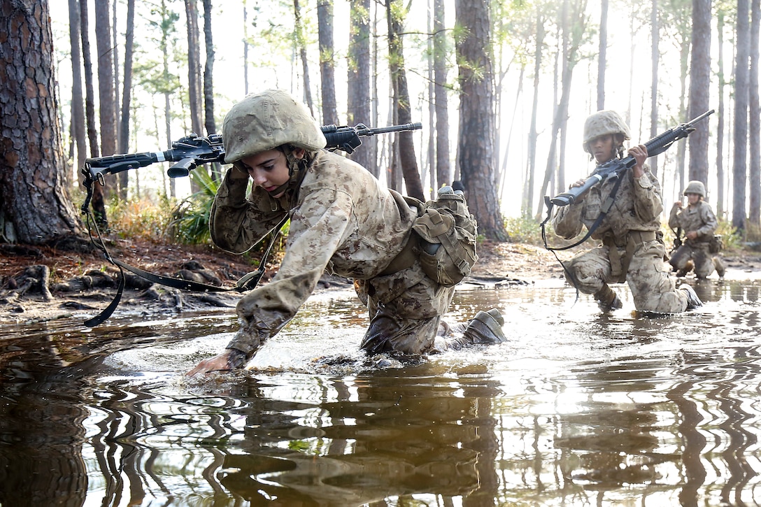 Three Marine Corps recruits crawl through water.