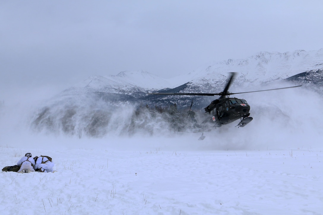 A helicopter hovers over a group of men in the snow.