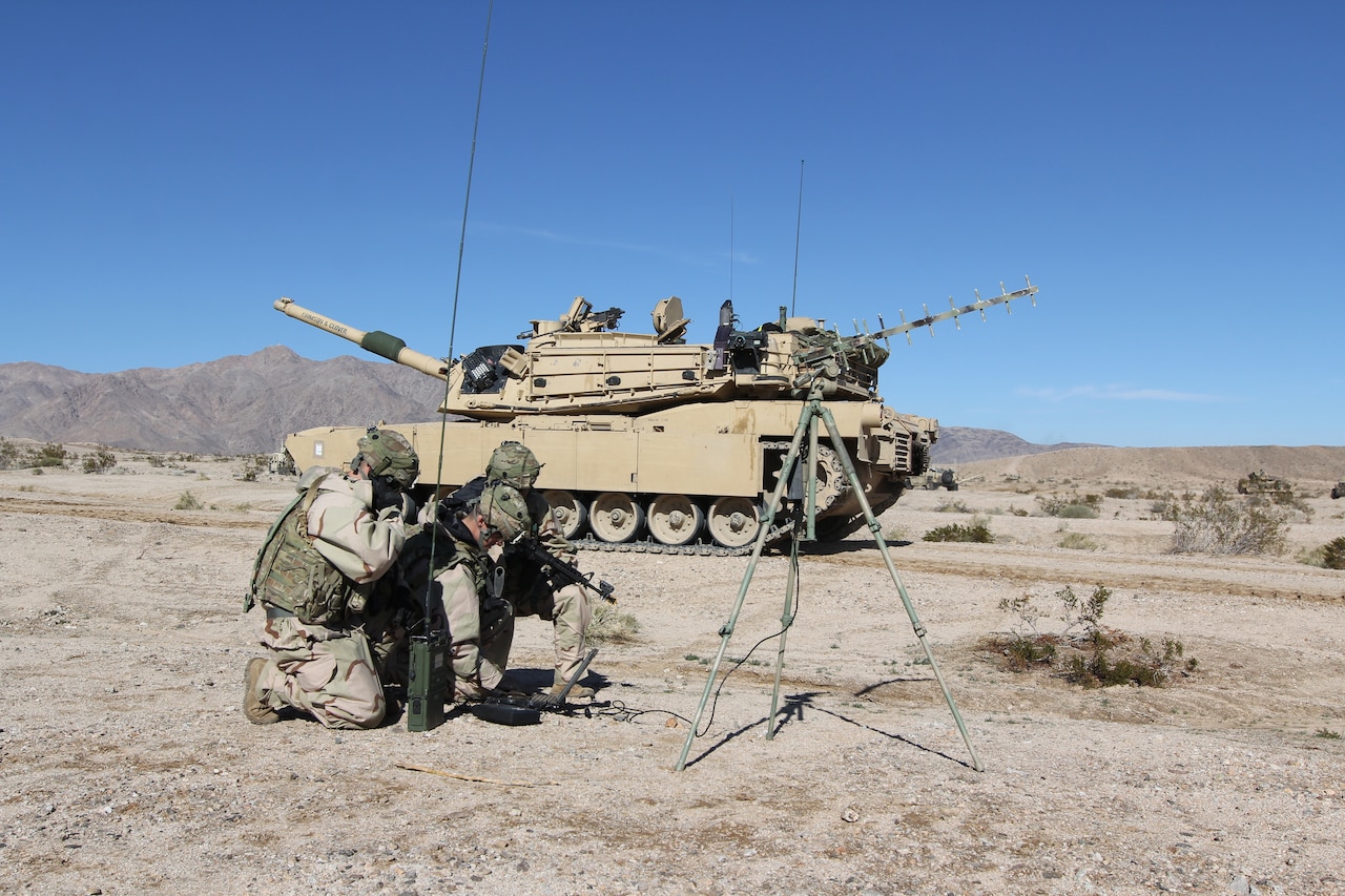 Soldiers crouch over gear in desert