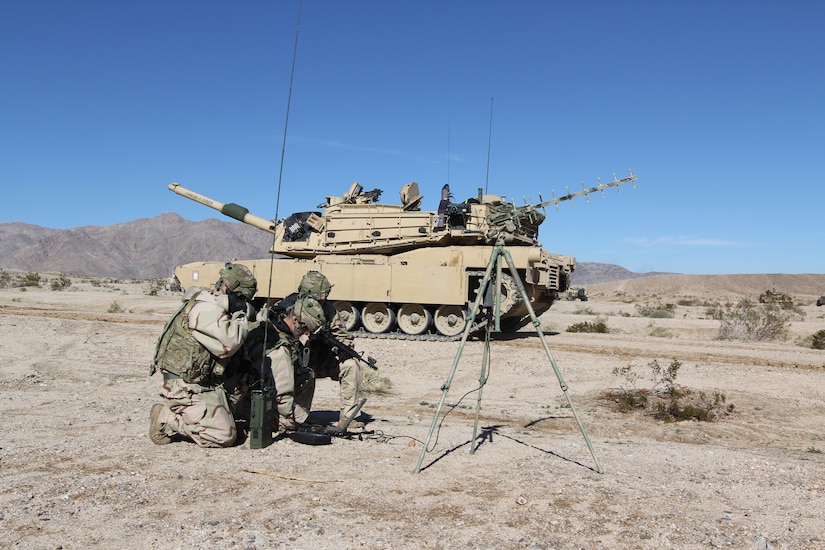 Soldiers crouch over gear in desert