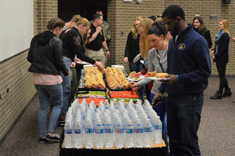 Students enjoying a catered lunch from Subway provided by the Springfield Army Recruiting Station. There is a table with students on both sides of it putting food on their plates. There are vegetable toppings, subs and water on the table as well.