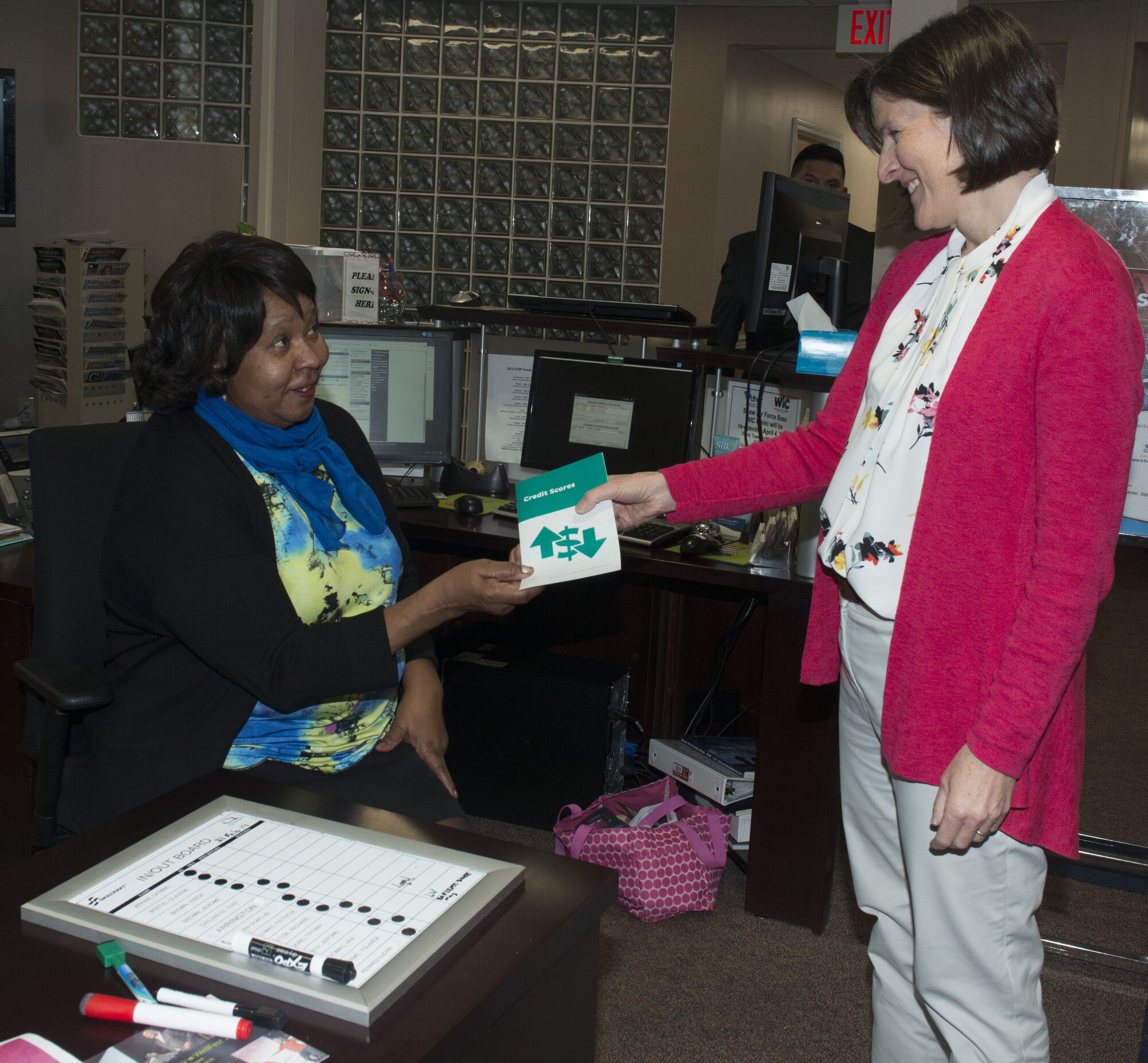 Arra Thomas, Airmen and Family Readiness Center personal financial readiness counselor, hands a credit score pamphlet to Dorcus Green, AFRC readiness consultant, at Shaw Air Force Base, S.C., Feb. 21, 2019.