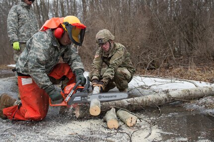 Spc. Kevin Morales assigned to Delta Company, 427th Brigade Support Battalion, 2nd Squadron, 101st Cavalry Regiment, New York Army National Guard, Buffalo cuts into a log with a chainsaw, while Spc. Ethan Brown assigned to Bravo Troop, 2nd Squadron, 101st Cavalry Regiment, assists him during training at Youngstown Local Training Area, Feb. 24, 2019.