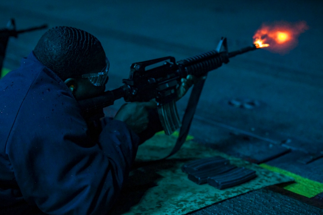 A sailor fires a weapon while he lies on the ground .