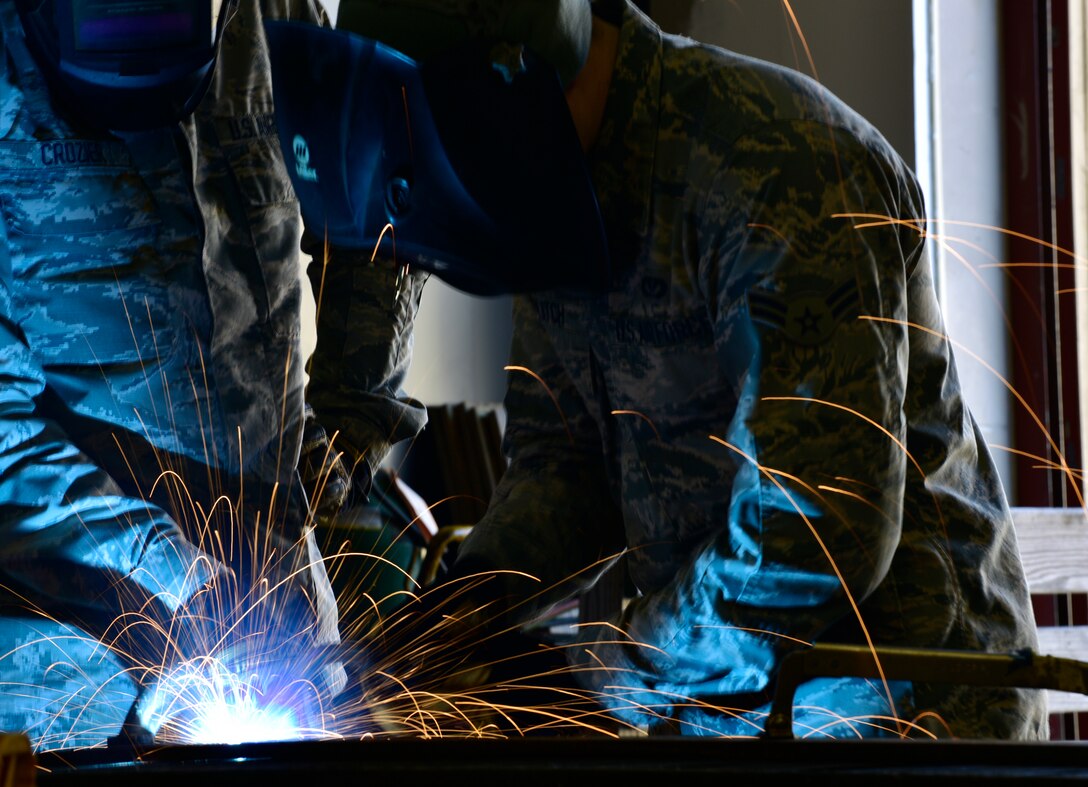 Two Airman weld a metal grate