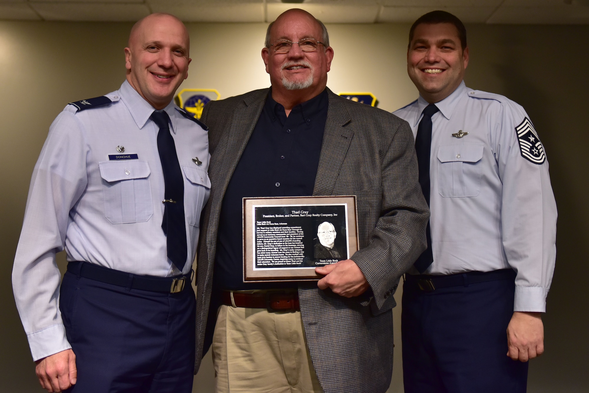 Two men in the Air Force blues uniform stand beside a man holding the Little Rock AFB Community Council Cornerstone award for 2018.