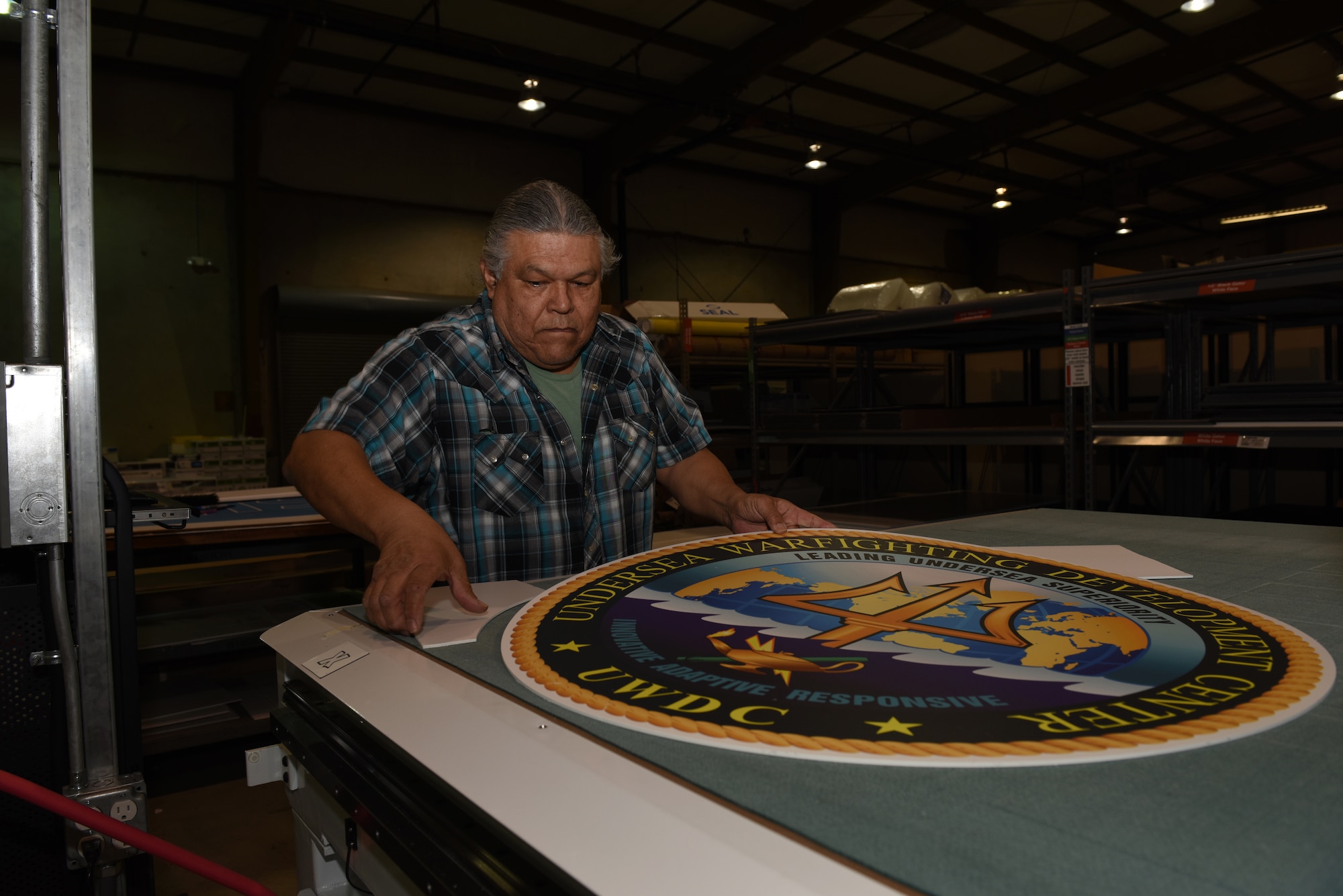Carlos Castro, Defense Logistics Agency, showcases a large decal Feb. 7, 2019, at Travis Air Force Base, Calif., after the decal was cut by a flatbed cutter. The Travis DLA facility provides a variety of printing services to federal agencies and government offices. (U.S. Air Force photo by Tech. Sgt. James Hodgman)