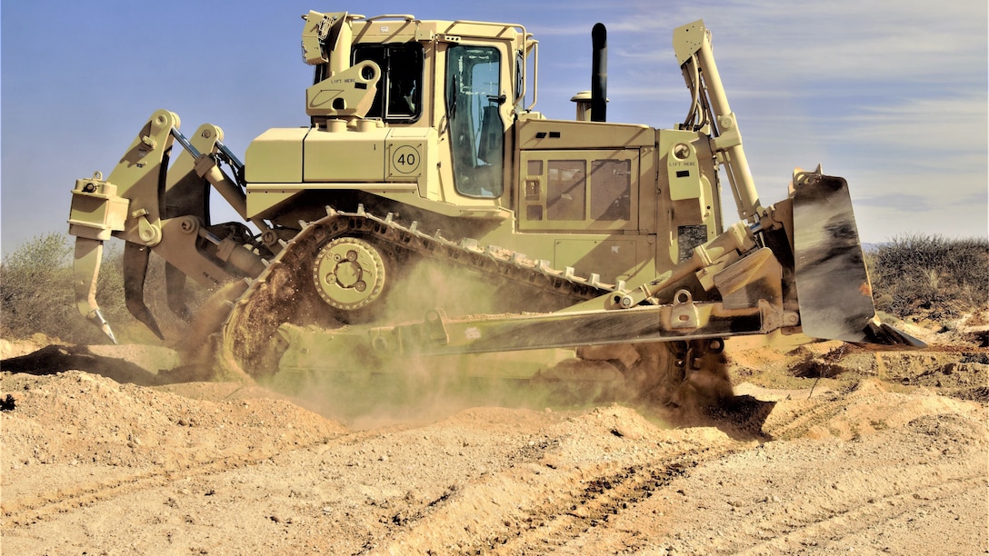 An armored bulldozer rolls through sandy terrain