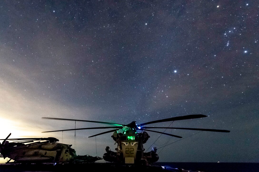 A helicopter sits parked at night underneath the stars.