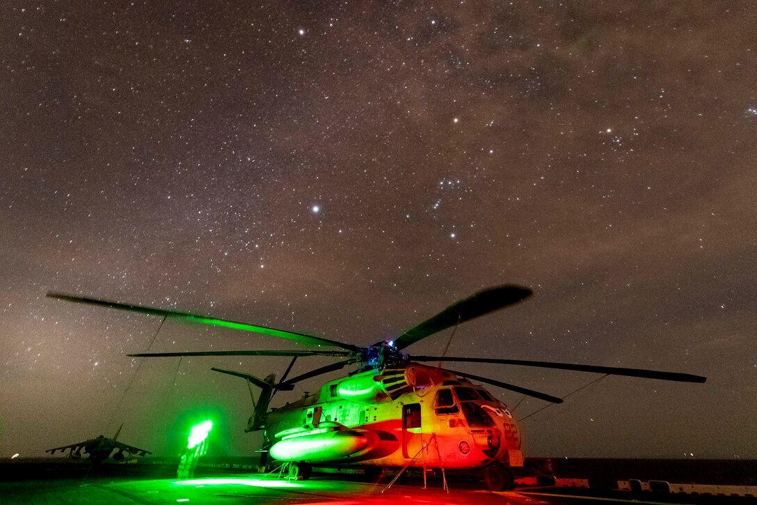 A helicopter with a green light shinning on one side sits parked at night underneath the stars.