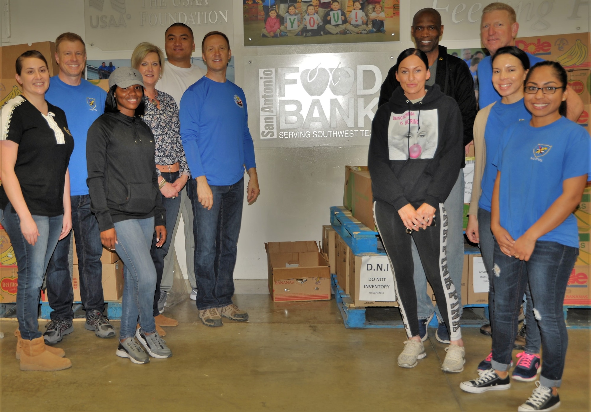 Headquarters 340 Flying Training Group Airmen and family members pose at the SA Foodbank in front of a nearly empty space, previously filled with cartons and bins and boxes and palettes of food waiting to be sorted. The team helped sort 10,000-plus pounds of food, representing more than 8,300 meals. Pictured are (left side, left to right) Tech. Sgt. Kassandra Farani, Col. Allen Duckworth, Tech. Sgt. Shakeeta Thomas, Jeanne Goetze, Tech. Sgt. Amosa Farani and Chief Master Sgt. Scott Goetze, and (right side, right to left, front row), Master Sgt. Natasha Todd, Master Sgt. Angelina Manby, and Tech. Sgt. Jaclyn Johnson, and (back row, right to left) Senior Master Sgt. Craig Pfister and Senior Master Sgt. Kwame Tawiah. Not pictured: Master Sgt. Faith Wells. (U.S. Air Force photo by Debbie Gildea)