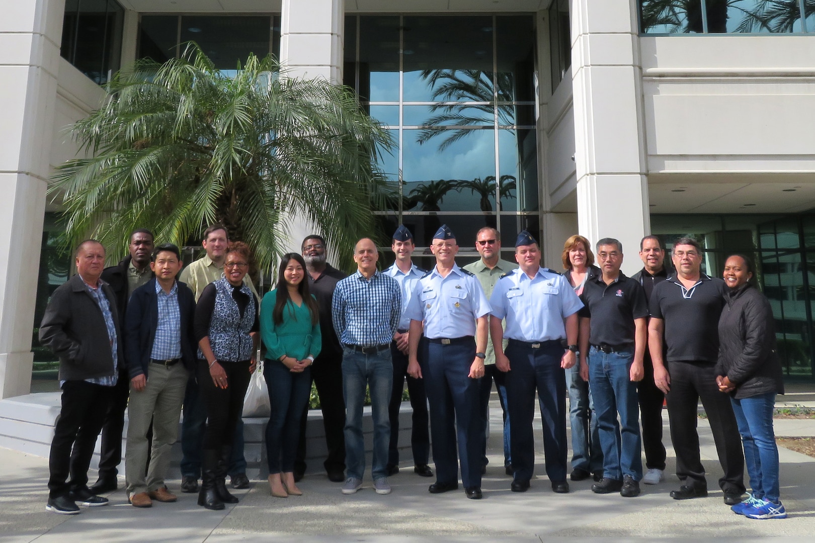 A group of civilian and military personnel stand before a building in group.