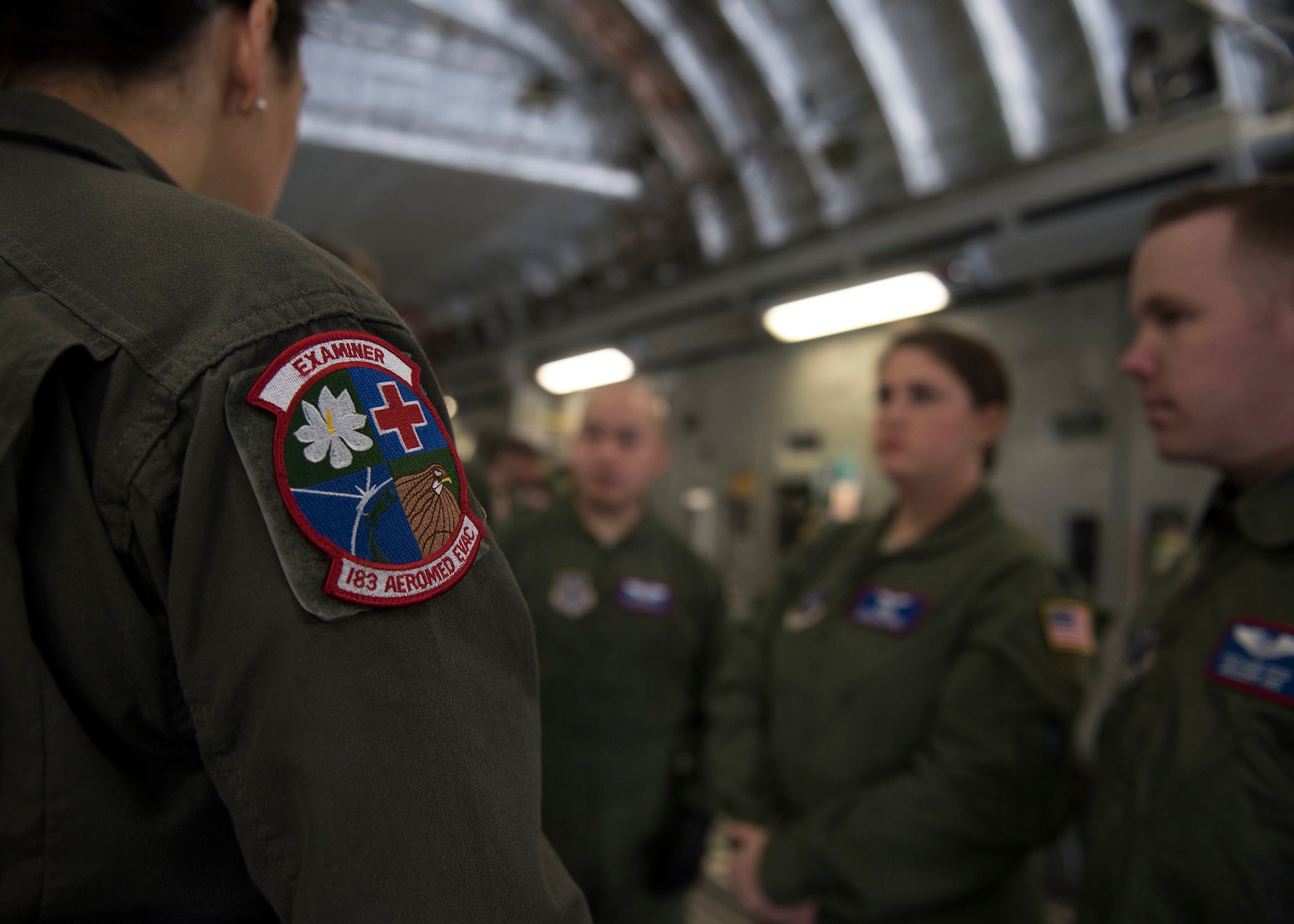 A 183rd Air Evacuation Squadron patch sits on an Airman's flight suit. in front of three Airmen.