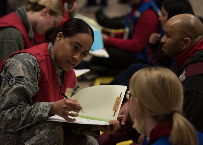 An Airman holds an open folder while speaking to a civilian.