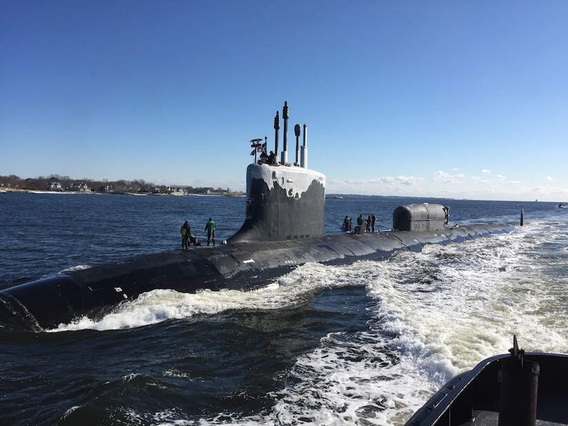 Sailors stand atop a submarine as it heads to port.