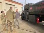 three people in uniform stand in front of a fuel truck