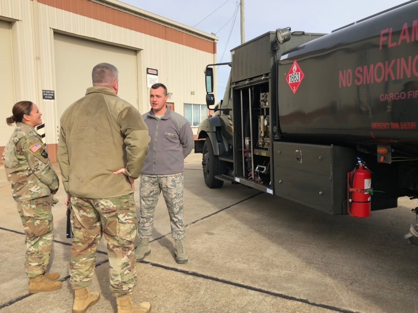 three people in uniform stand in front of a fuel truck