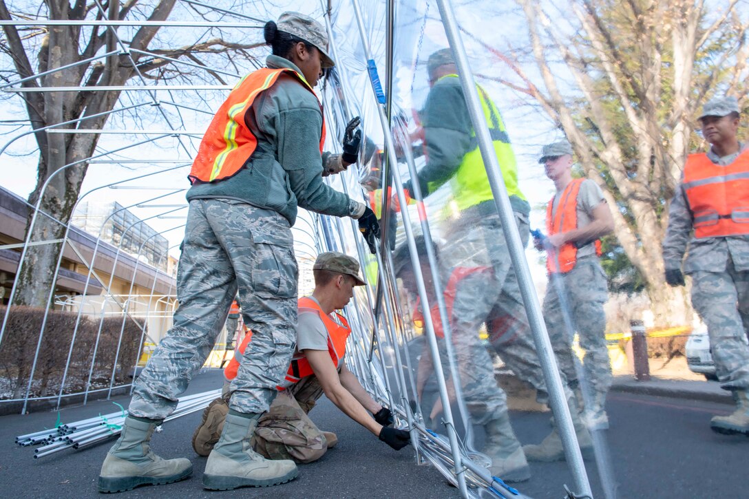 A group of airman lift up a plastic wall.