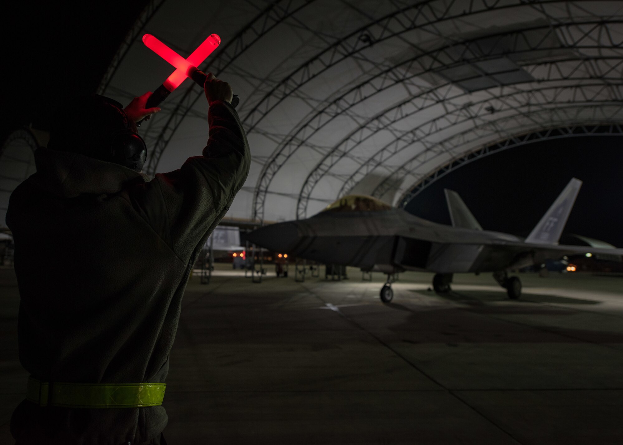 U.S. Air Force Airman 1st Class Alan Bernal, 1st Aircraft Maintenance Squadron assistant dedicated crew chief, guides an F-22 Raptor pilot under a sunshade at Joint Base Langley-Eustis, Virginia, Feb. 21, 2018.