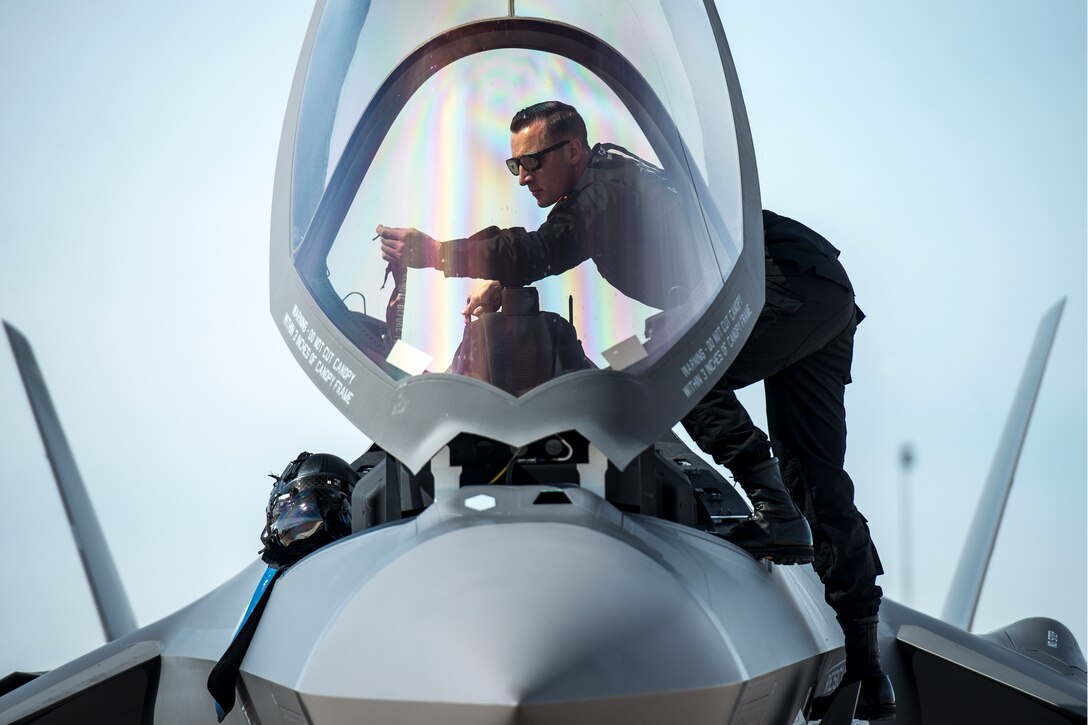 An airman stands behind the canopy of a jet.