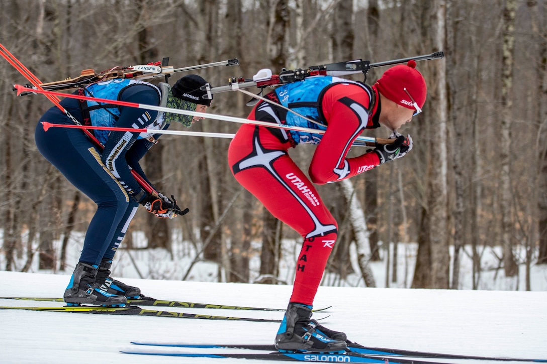 Two soldiers cross-country ski in a forested area.