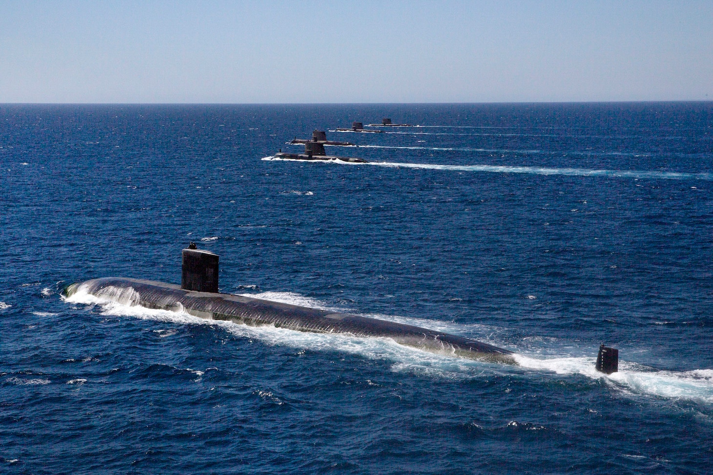 Five submarines sail across water.