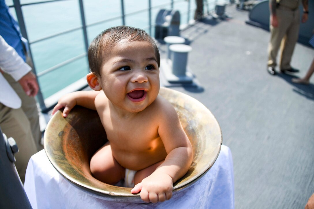 A toddler sits in a bell on a ship.