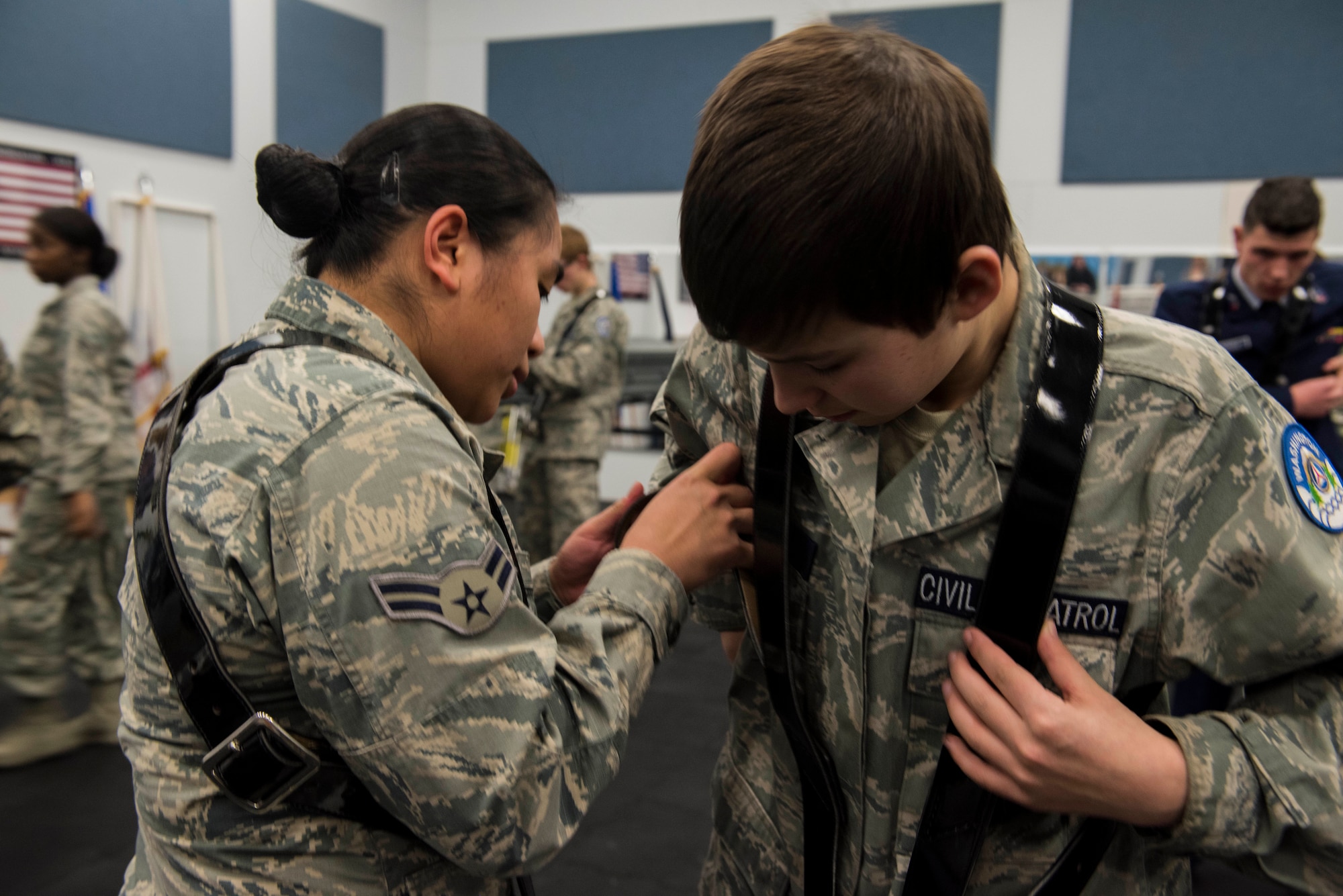 U.S. Air Force Airman 1st Class Larrah Lara, 92nd Air Refueling Wing base honor guardsman, assists Civil Air Patrol Cadet Routh, 21st Fairchild Composite Squadron, with attaching a harness used to carry flag during color guard ceremonies at Fairchild Air Force Base, Washington, Feb. 26, 2019. CAP is a volunteer organization with an aviation-minded membership that includes people from all backgrounds, lifestyles and occupations. (U.S. Air Force Photo by Airman 1st Class Lawrence Sena)