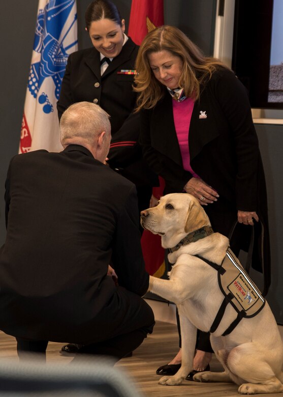 A man kneels to appoint a service dog as honorary hospital corpsman.