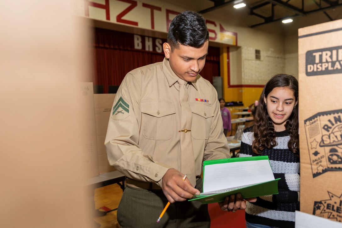 Lance Cpl. Jose Corpus, ammunition technician specialist, reviews the grading rubric while discussing a project with a student at the STEAM Fair aboard Barstow High School, Barstow, Calif., Feb. 21. (U.S. Marine Corps Photo by Jack J. Adamyk)