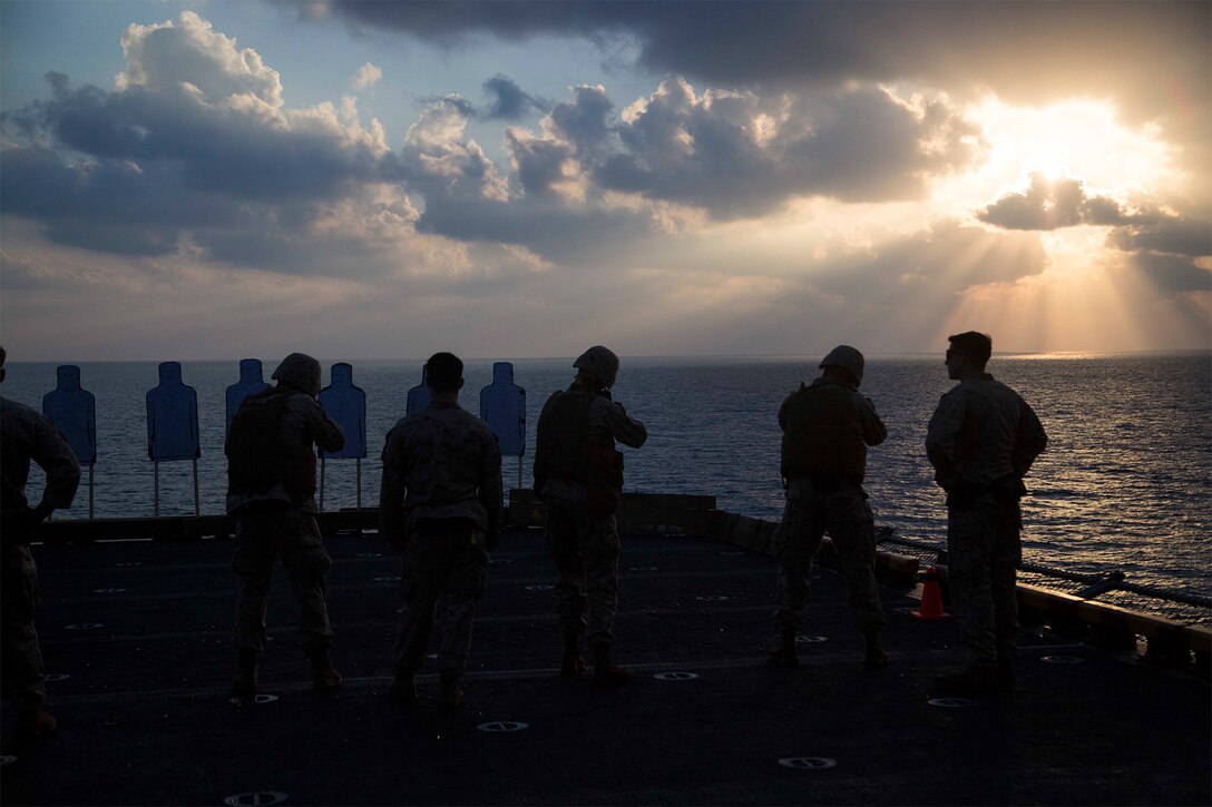 A group of Marines fire on training targets from the deck of a ship.