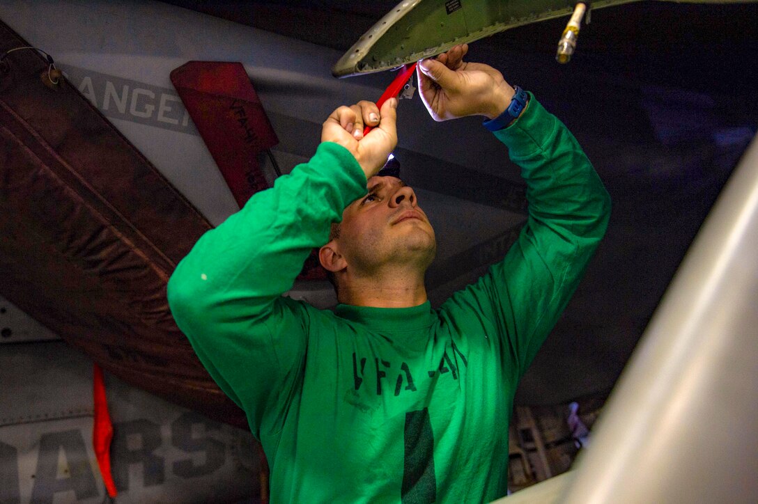 A sailor uses a small hand tool to remove sealant from an aircraft.