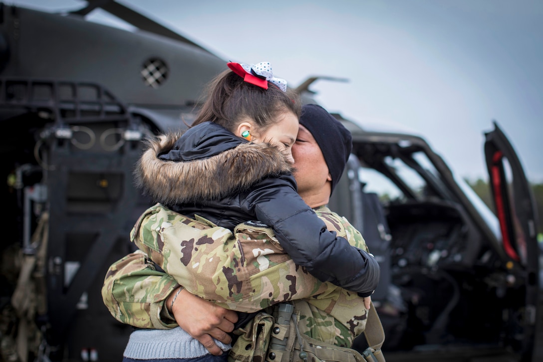 A soldier embraces his daughter next to an aircraft.