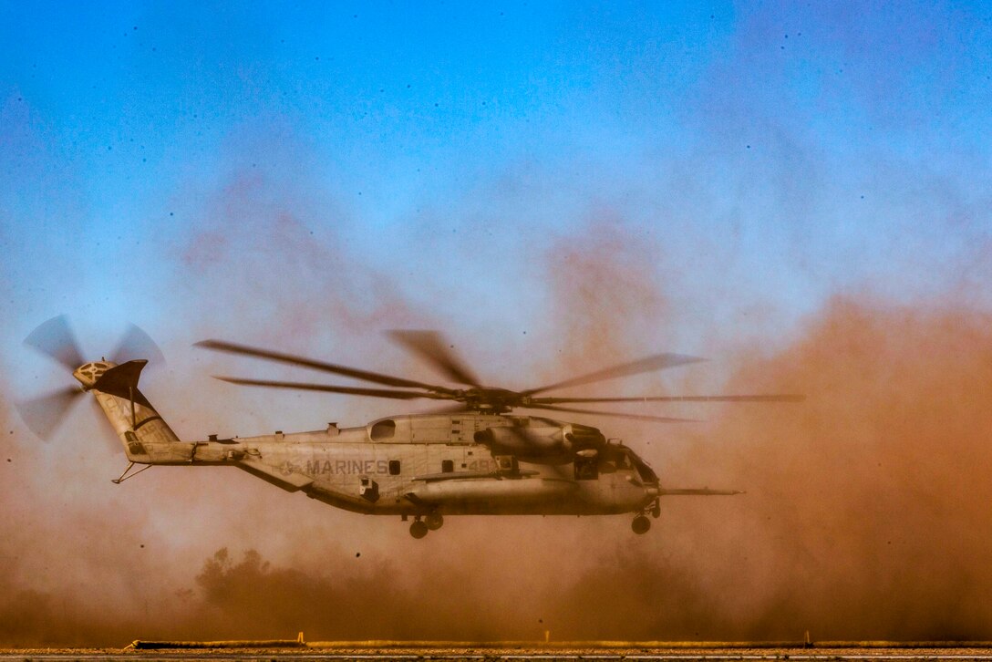 A helicopter takes off, scattering a cloud of dust.