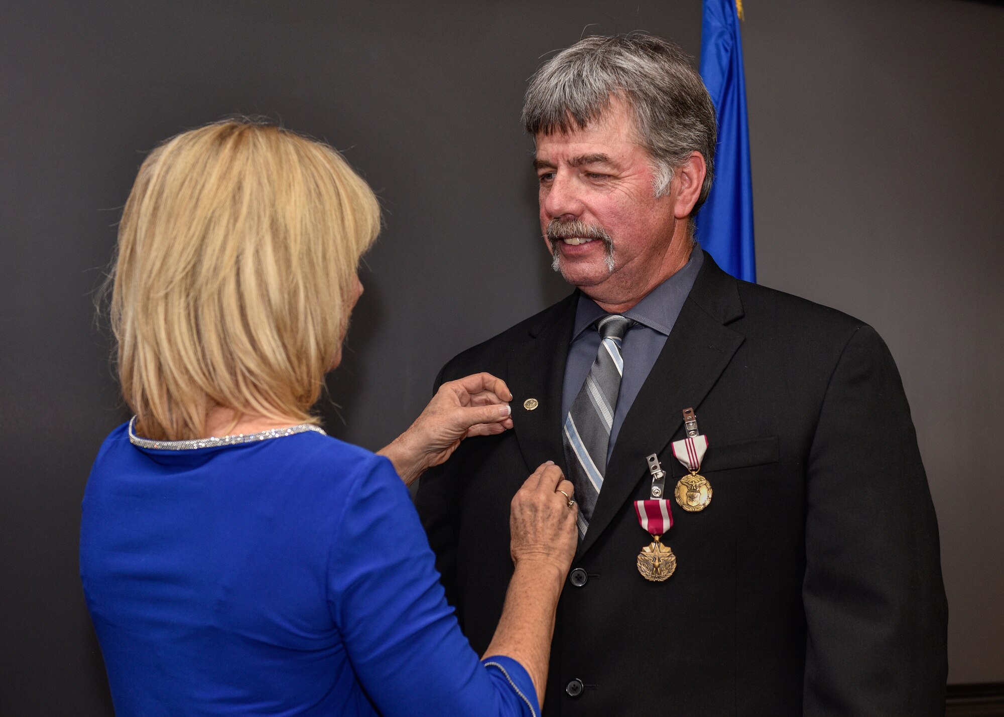 Joseph Nevins, 58th Maintenance Group deputy director, is given his retirement pin by his wife Lisa at Kirtland Air Force Base, N.M., Jan. 4, 2019. Nevins served his country both as an Airman and as a civil servant with nearly 43 years of service. Nevins has served as the 58th Maintenance Group deputy director here from 2004-2019, where he directed and integrated the efforts of 936 personnel supporting the execution of a 12,000 hour annual flying program for the Air Education and Training Command formal aircrew training schools for special forces and air rescue personnel. (U.S. Air Force photo by Airman 1st Class Austin J. Prisbrey)