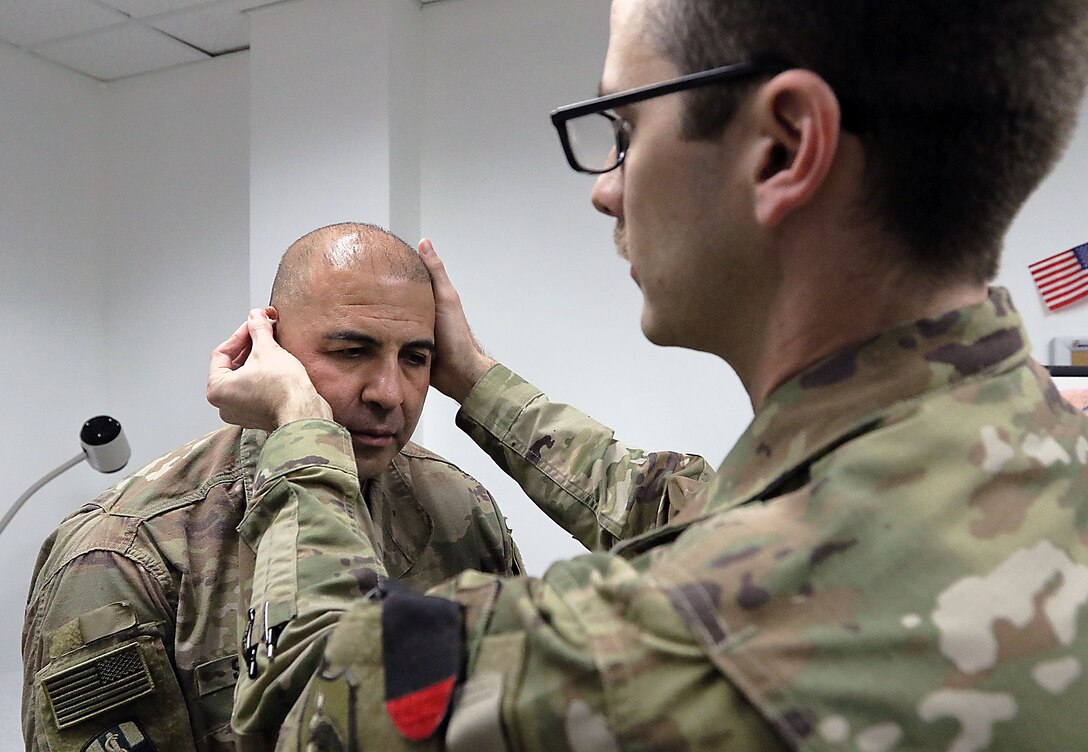 Air Force Dr. (Capt.) Carl Bryce places a Battlefield Acupuncture needle into the outer ear area of Chief Warrant Office 2 George Scott.