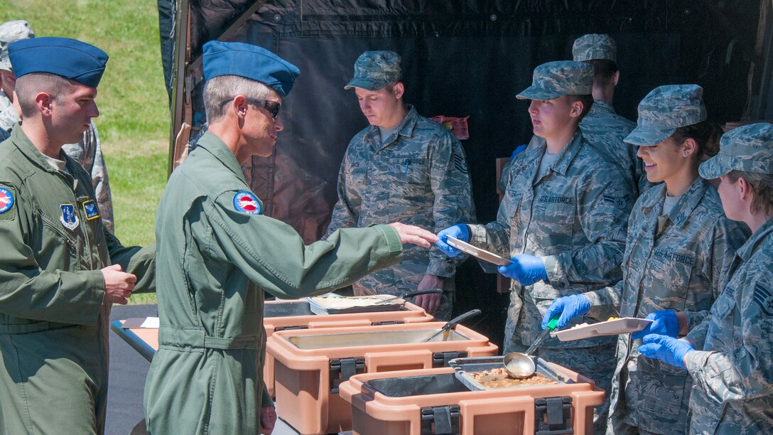 Airmen receive unit group ration food from a food service line outside at a Single Pallet Expeditionary Kitchen