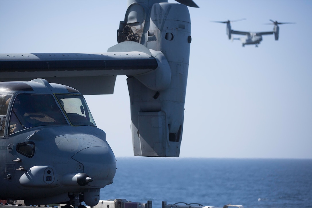 Two Marine Corps Osprey aircraft land on a ship.