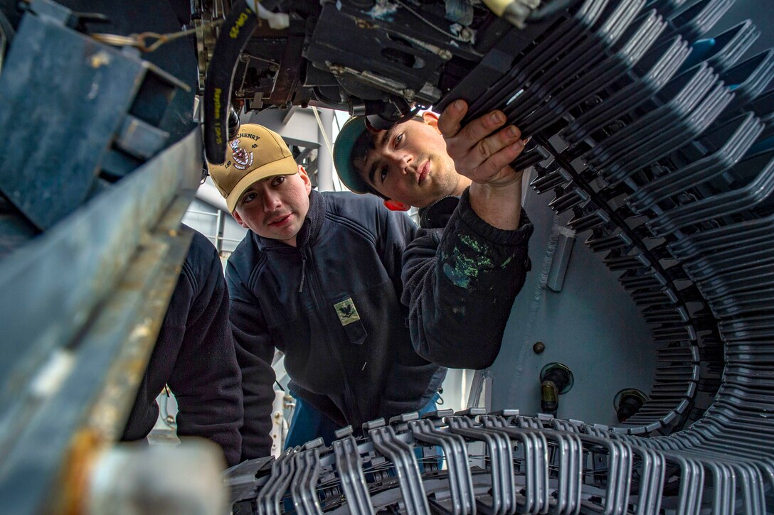 Sailors check a large machine gun.