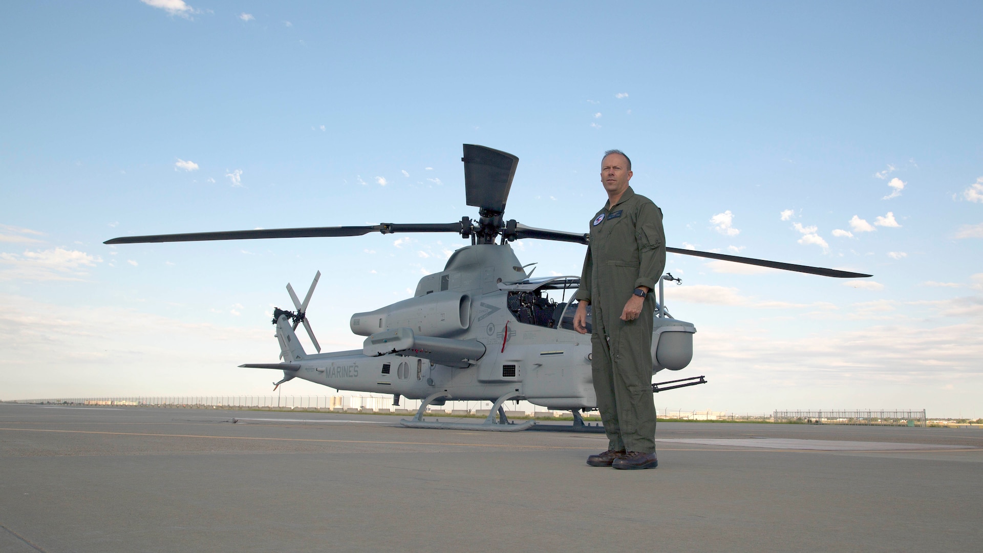 Marine pilot stands in front of a AH-1Z Viper on a flight line.