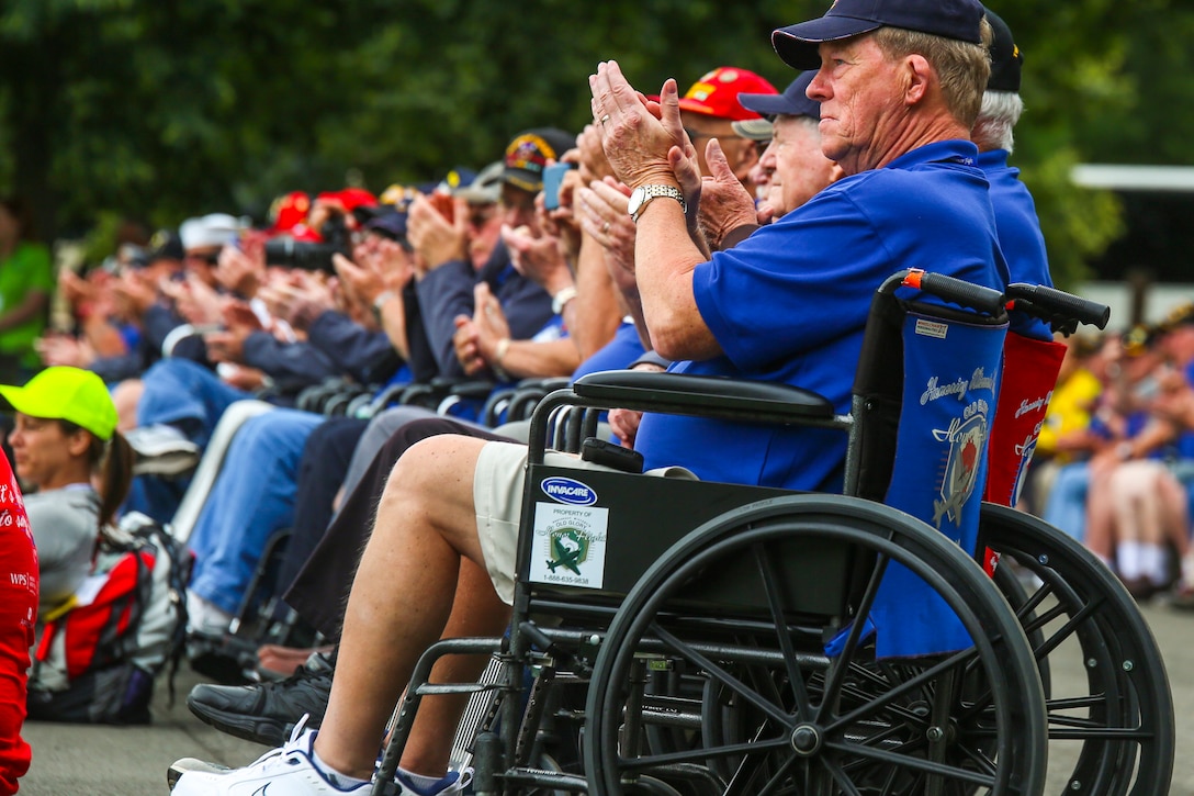 A group or veterans sitting in wheelchairs clap.