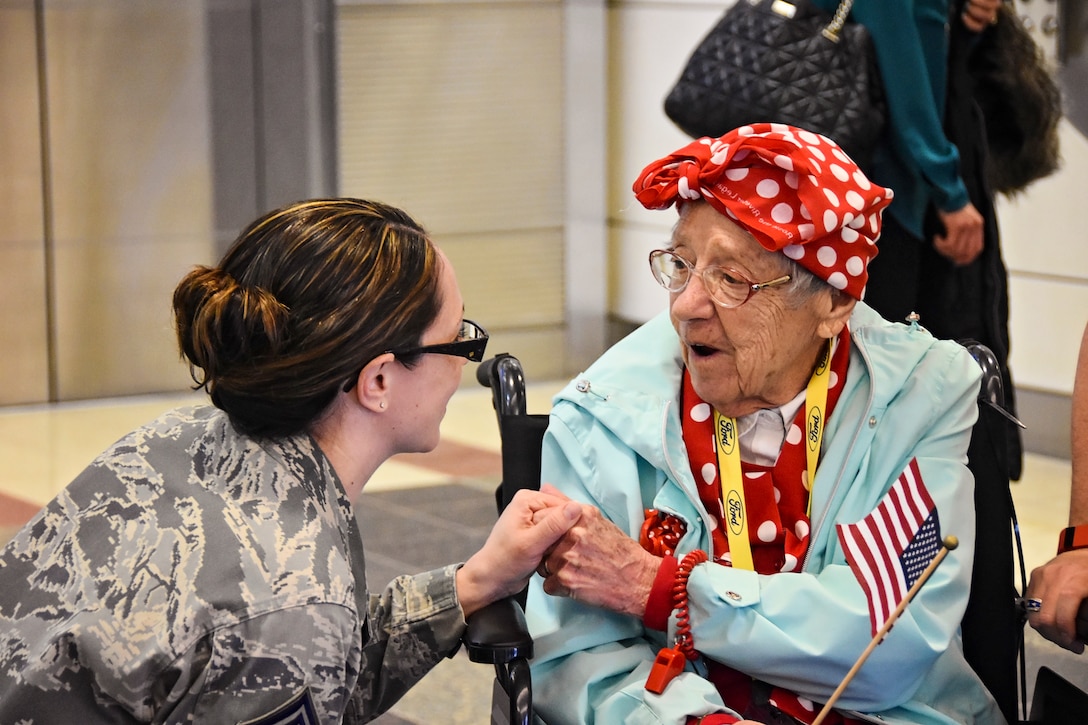 A woman kneels beside another woman sitting in a wheelchair.