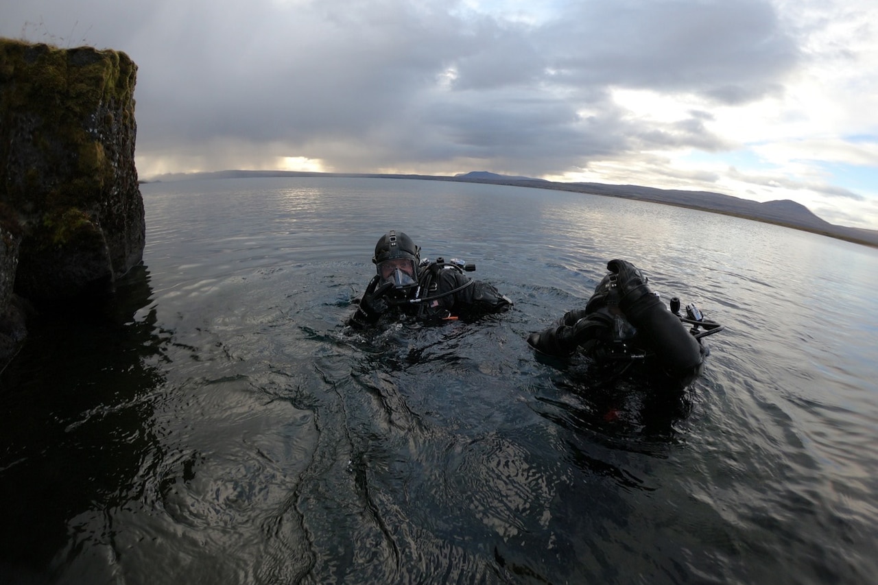 Sailors in scuba gear prepare to depart the ocean.