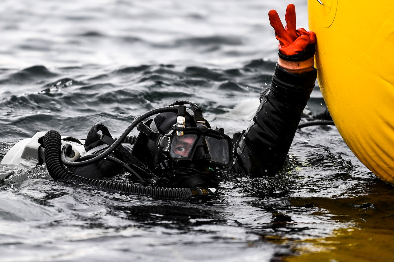 Sailor in dive gear hand signals while in the ocean.