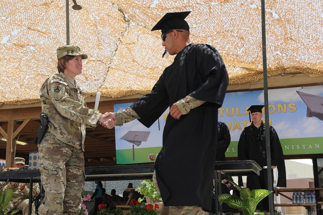 A man in a cap and gown shakes hands with an Army general on a graduation stage.